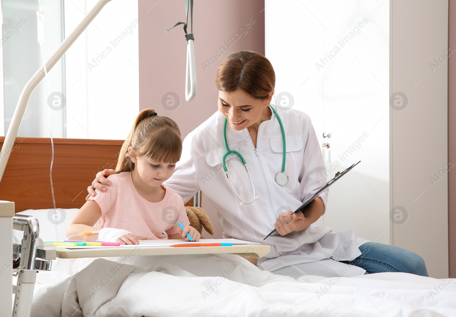 Photo of Little child with intravenous drip drawing in hospital bed during doctor's visit