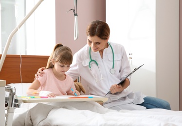 Little child with intravenous drip drawing in hospital bed during doctor's visit