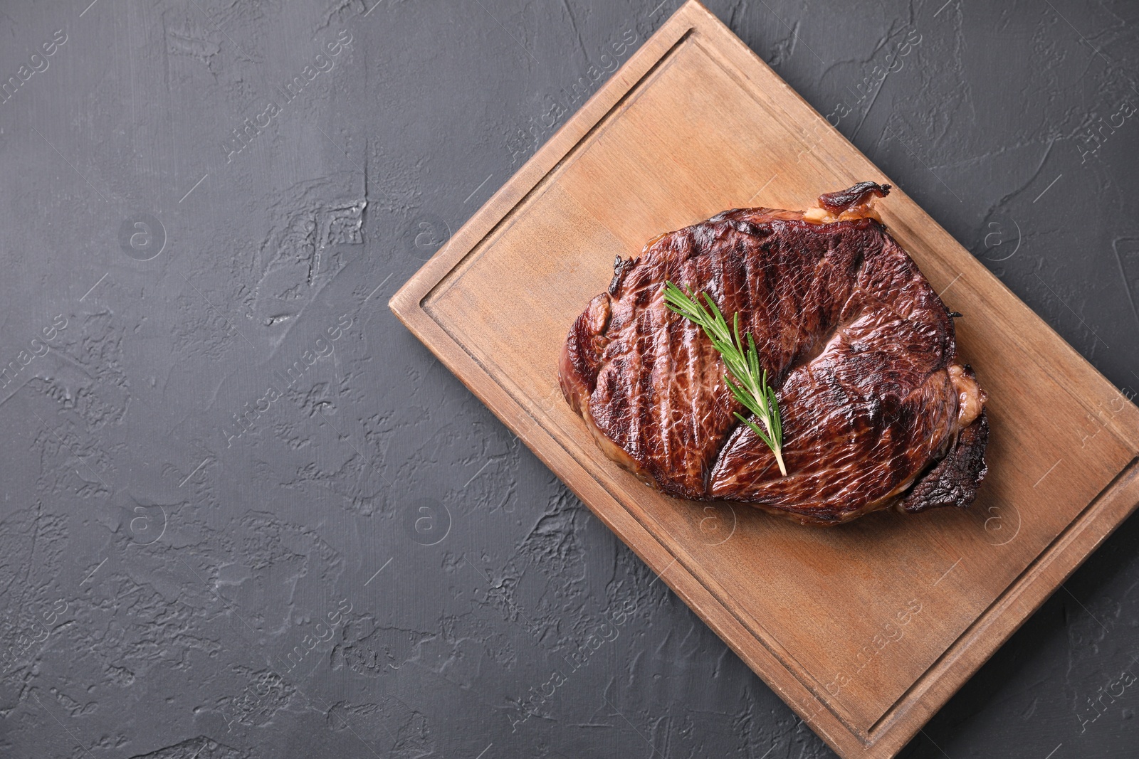 Photo of Wooden board with delicious fried beef meat and rosemary on grey textured table, top view. Space for text