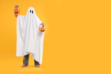 Photo of Woman in white ghost costume holding pumpkin buckets on yellow background, space for text. Halloween celebration