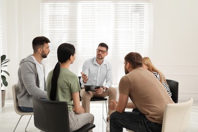 Psychotherapist working with group of drug addicted people at therapy session indoors