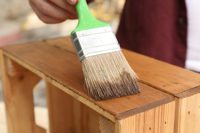 Photo of Man applying wood stain onto crate against blurred background, closeup