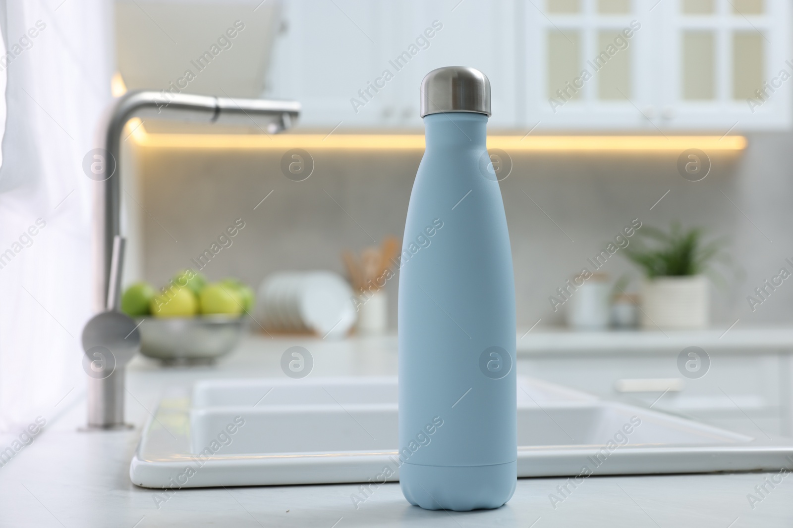 Photo of Stylish thermo bottle on white countertop in kitchen. Space for text