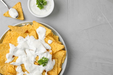 Plate of Mexican nacho chips with sauce on grey stone background, flat lay. Space for text