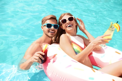 Photo of Young couple with cocktails in pool on sunny day