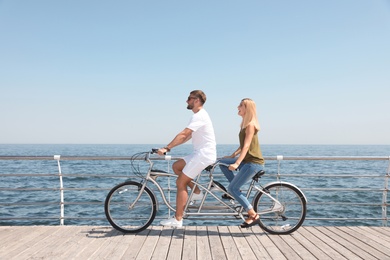 Couple riding tandem bike near sea on sunny day