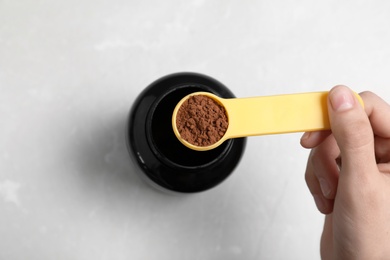 Man holding scoop of protein powder over jar on light background, top view