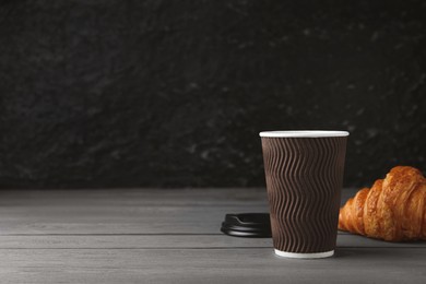 Coffee to go. Paper cup with tasty drink and croissant on grey wooden table. Space for text