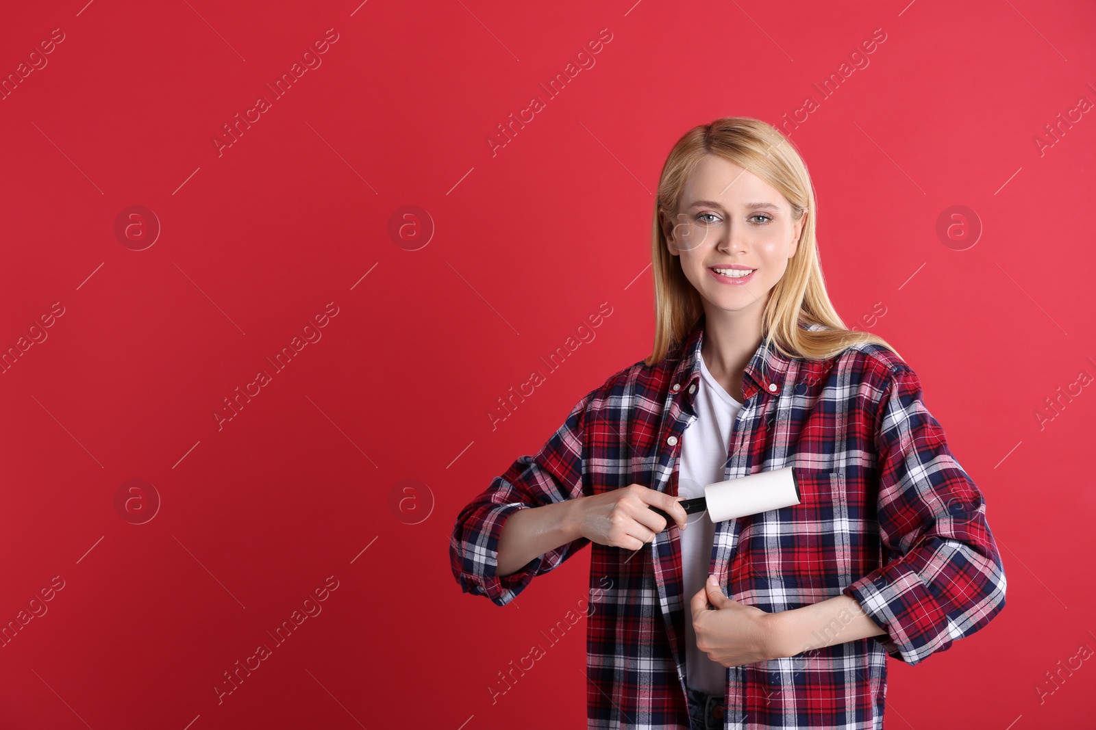 Photo of Young woman cleaning clothes with lint roller on red background. Space for text
