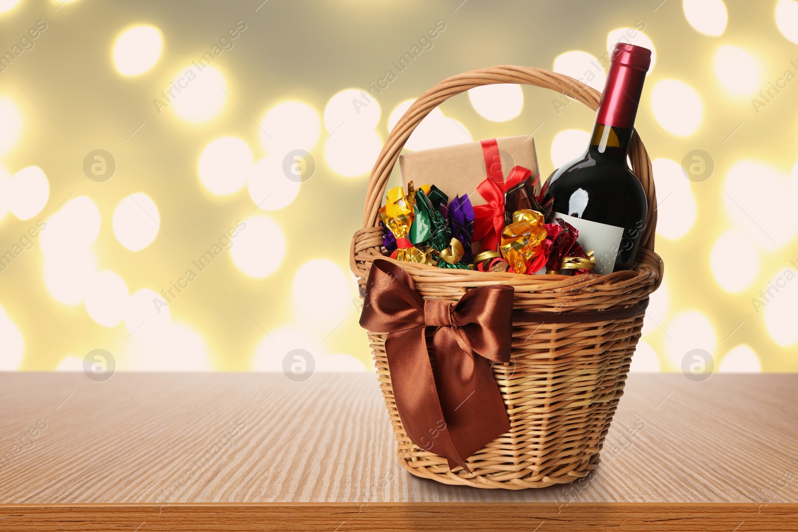 Image of Wicker basket full of gifts on table against blurred festive lights. Space for text