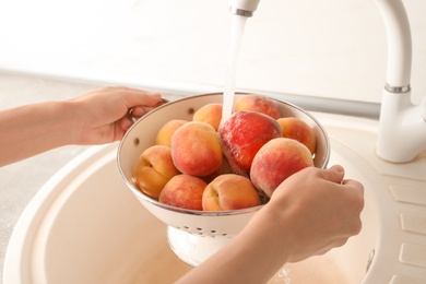 Photo of Woman washing fresh sweet peaches in kitchen