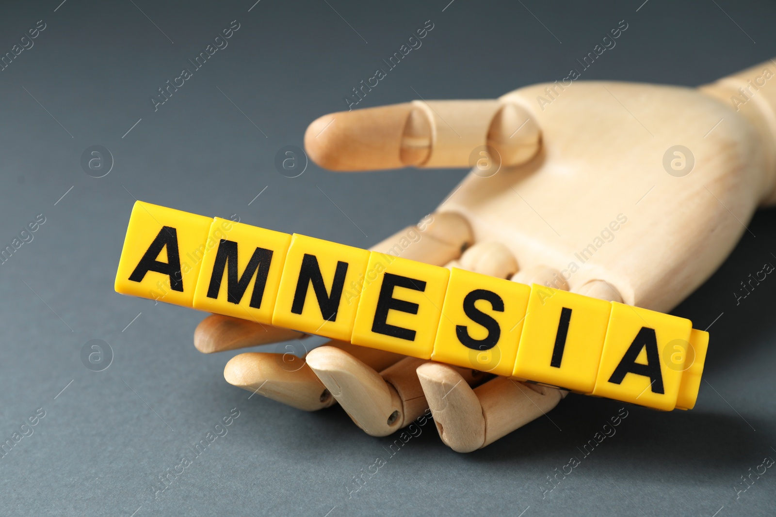 Photo of Amnesia. Mannequin hand with yellow cubes on grey background, closeup