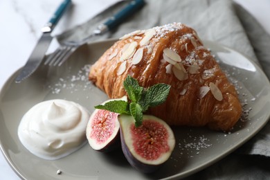 Photo of Delicious croissant with fig, almond flakes and cream on white table, closeup