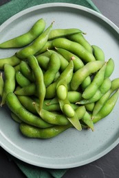 Plate of green edamame beans in pods on black table, top view