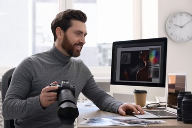 Photo of Professional photographer with digital camera using laptop at table in office