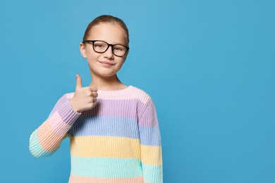 Cute girl in glasses showing thumb up on light blue background. Space for text