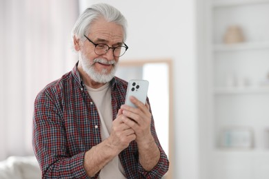 Portrait of happy grandpa with glasses using smartphone indoors