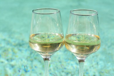 Photo of Glasses of tasty wine near swimming pool, closeup