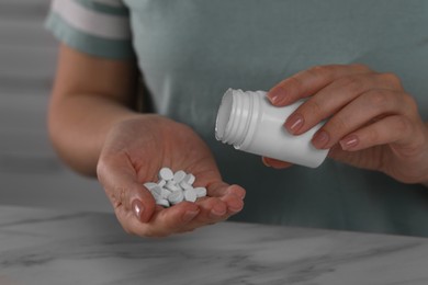 Photo of Woman pouring antidepressants from bottle at table, closeup