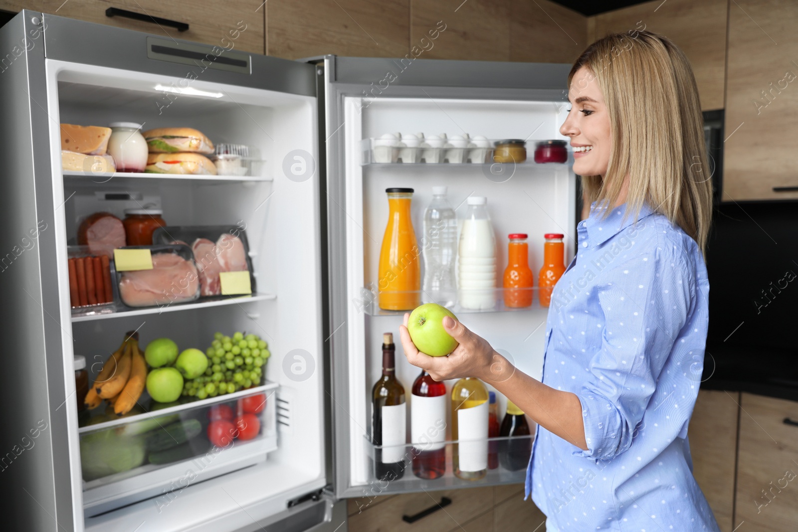 Photo of Woman with apple near refrigerator in kitchen