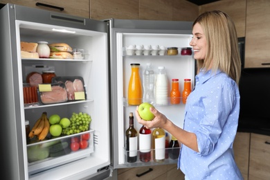 Woman with apple near refrigerator in kitchen
