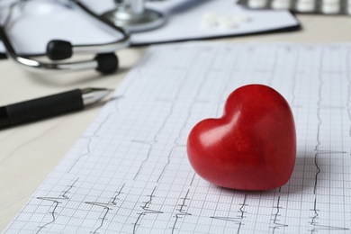 Photo of Cardiogram report and red decorative heart on table, closeup