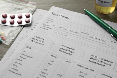 Photo of Drug test result form, pills, container with urine sample and pen on wooden table, closeup
