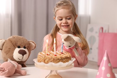 Photo of Cute girl with birthday cake and toys at table indoors