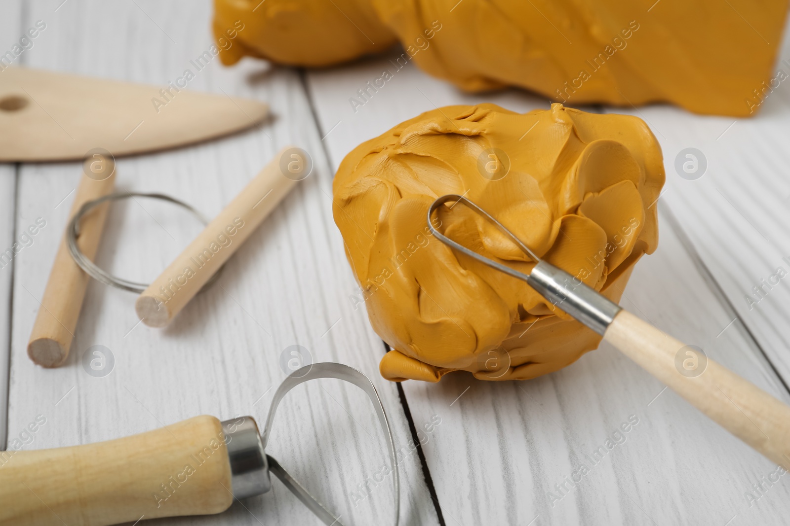 Photo of Clay and set of modeling tools on white wooden table, closeup