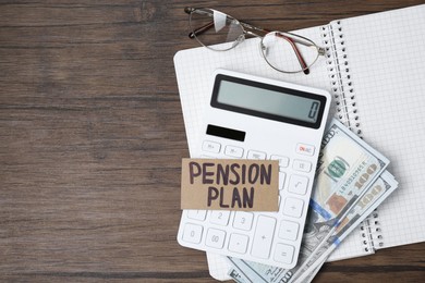 Photo of Card with phrase Pension Plan, calculator, dollar banknotes, notebook and glasses on wooden table, top view. Space for text