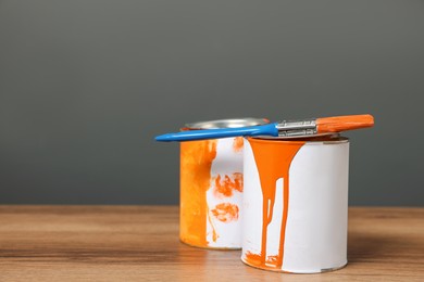 Photo of Cans of orange paint and brush on wooden table. Space for text
