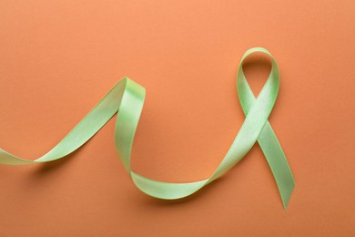 Photo of World Mental Health Day. Green ribbon on pale orange background, top view