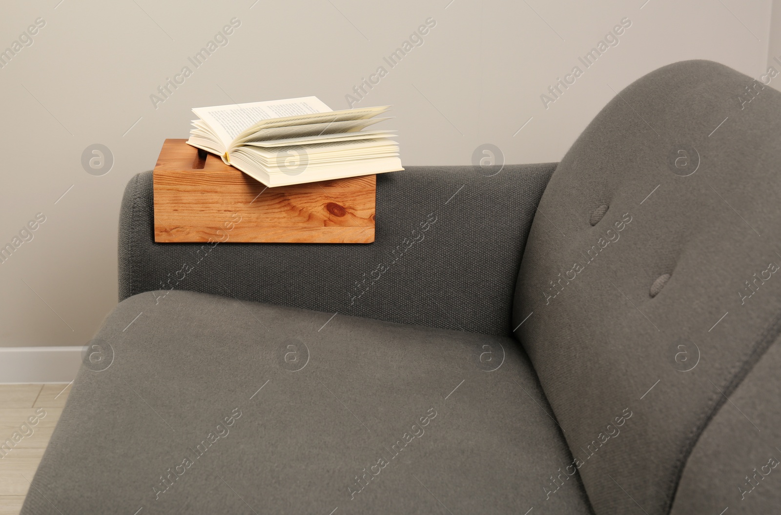 Photo of Open book on sofa with wooden armrest table in room. Interior element