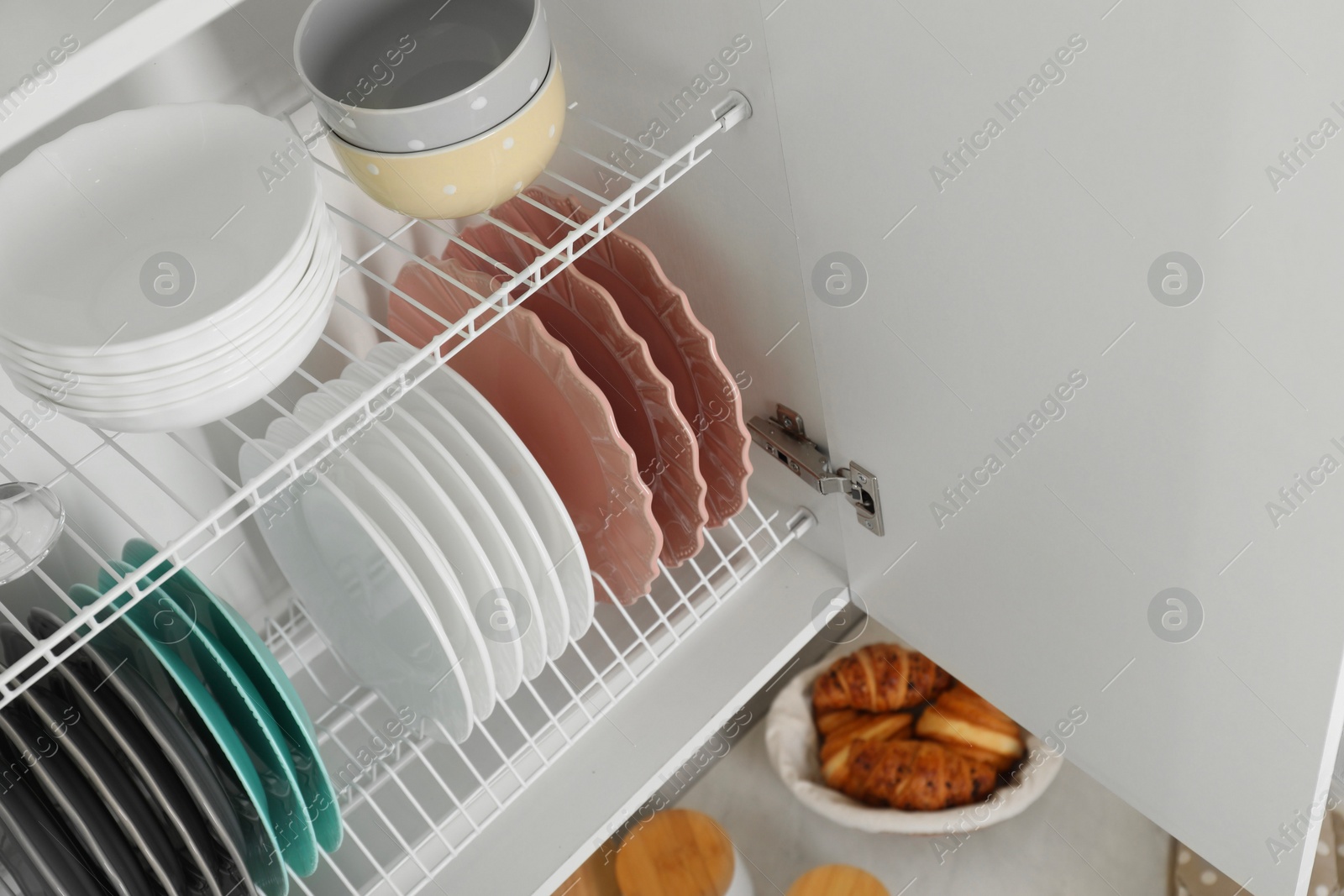 Photo of Clean plates and bowls on shelves in cabinet indoors