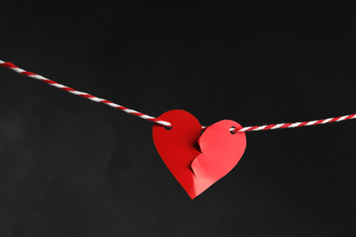 Photo of Broken red paper heart on rope against black background. Relationship problems concept