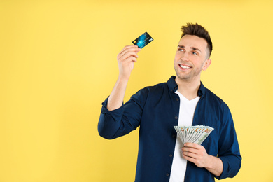 Photo of Happy man with cash money and credit card on yellow background
