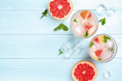 Photo of Flat lay composition of refreshing drink and grapefruits on light blue wooden table, space for text