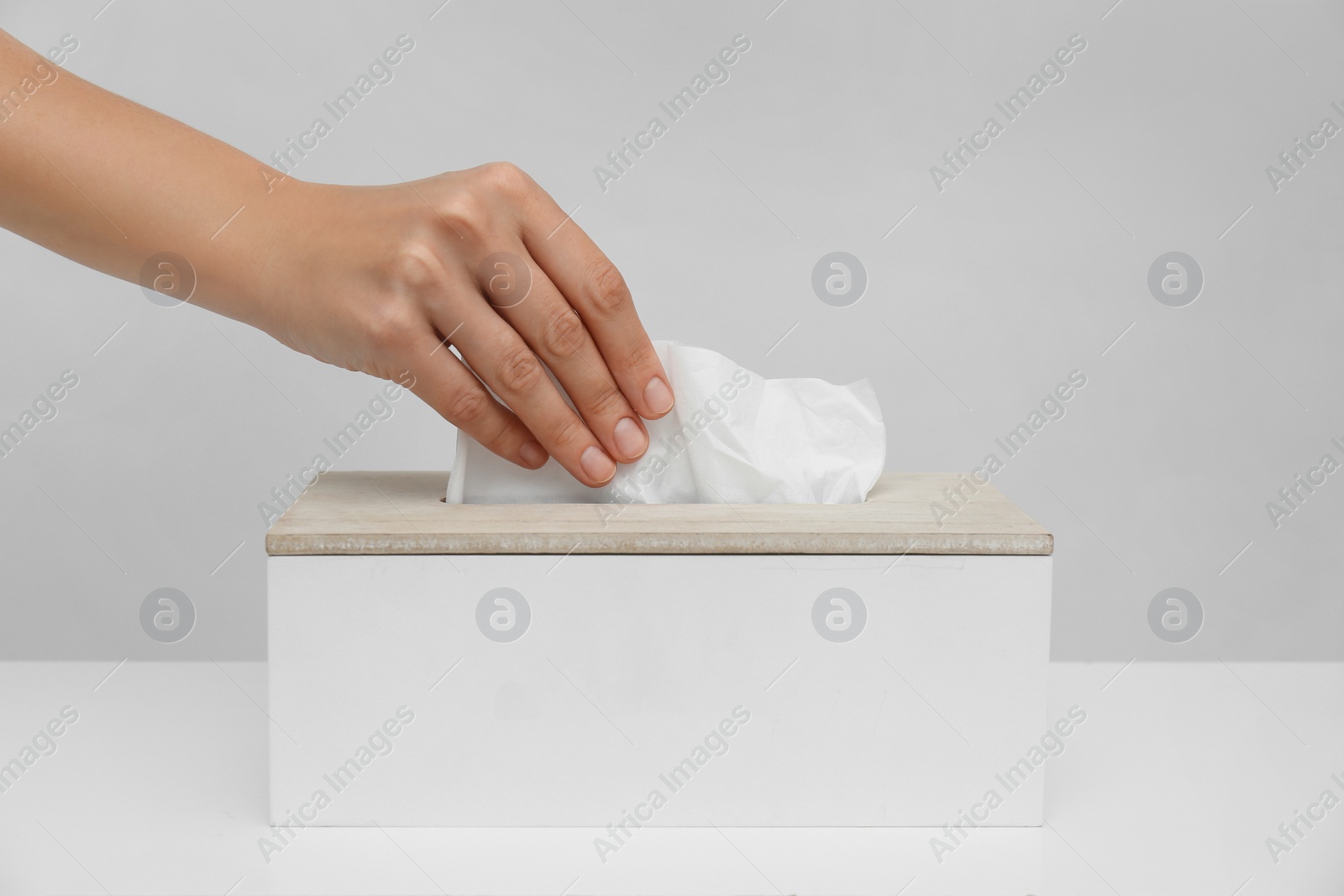 Photo of Woman taking paper tissue from holder on light background, closeup