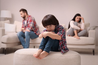 Photo of Sad little boy and his arguing parents on sofa in living room