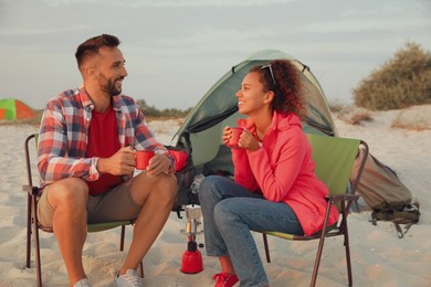 Couple with hot drinks on beach near camping tent
