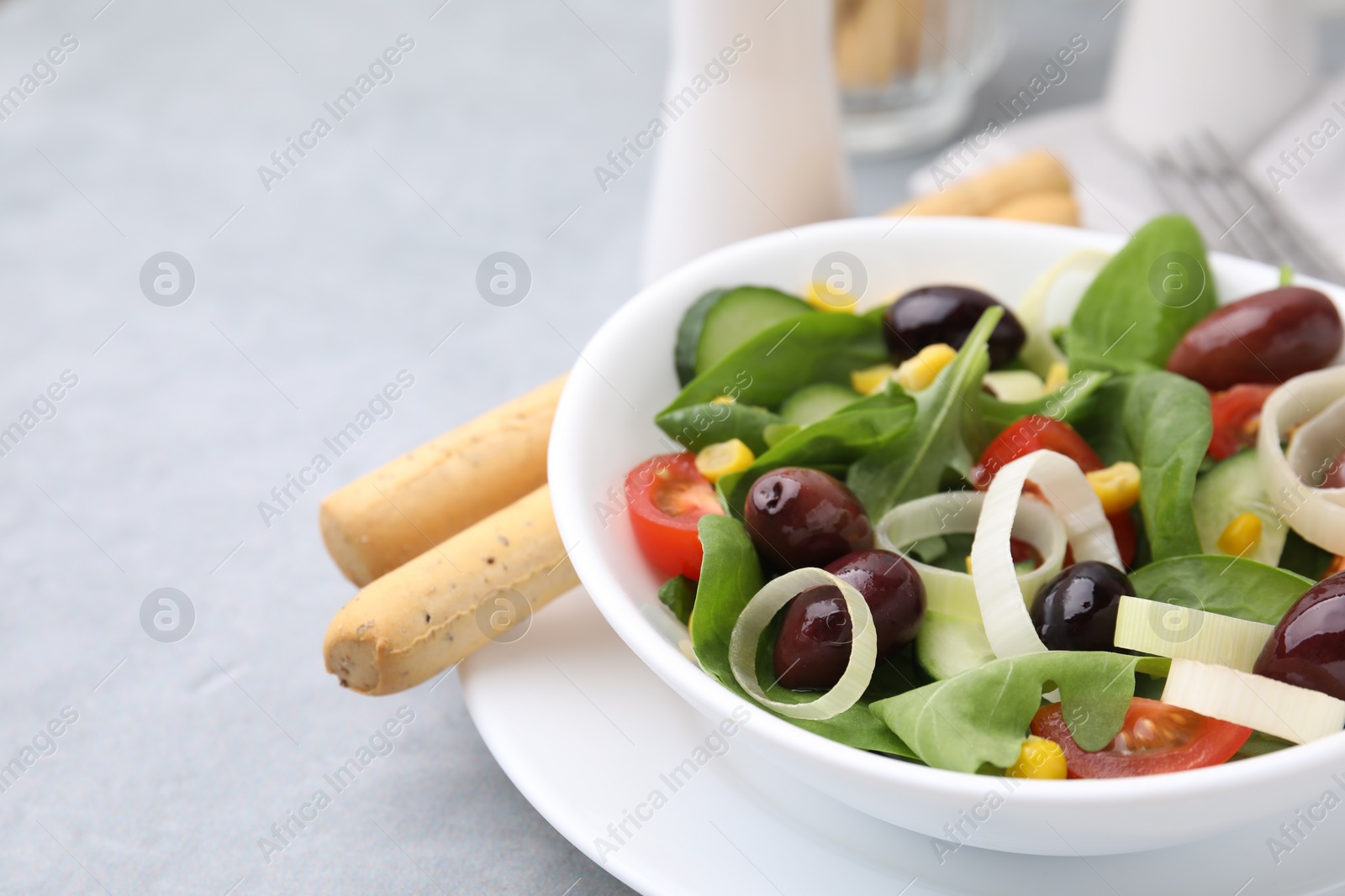 Photo of Bowl of tasty salad with leek and olives on grey table, closeup. Space for text