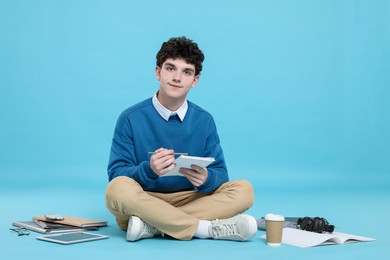 Portrait of student with notebook and stationery on light blue background