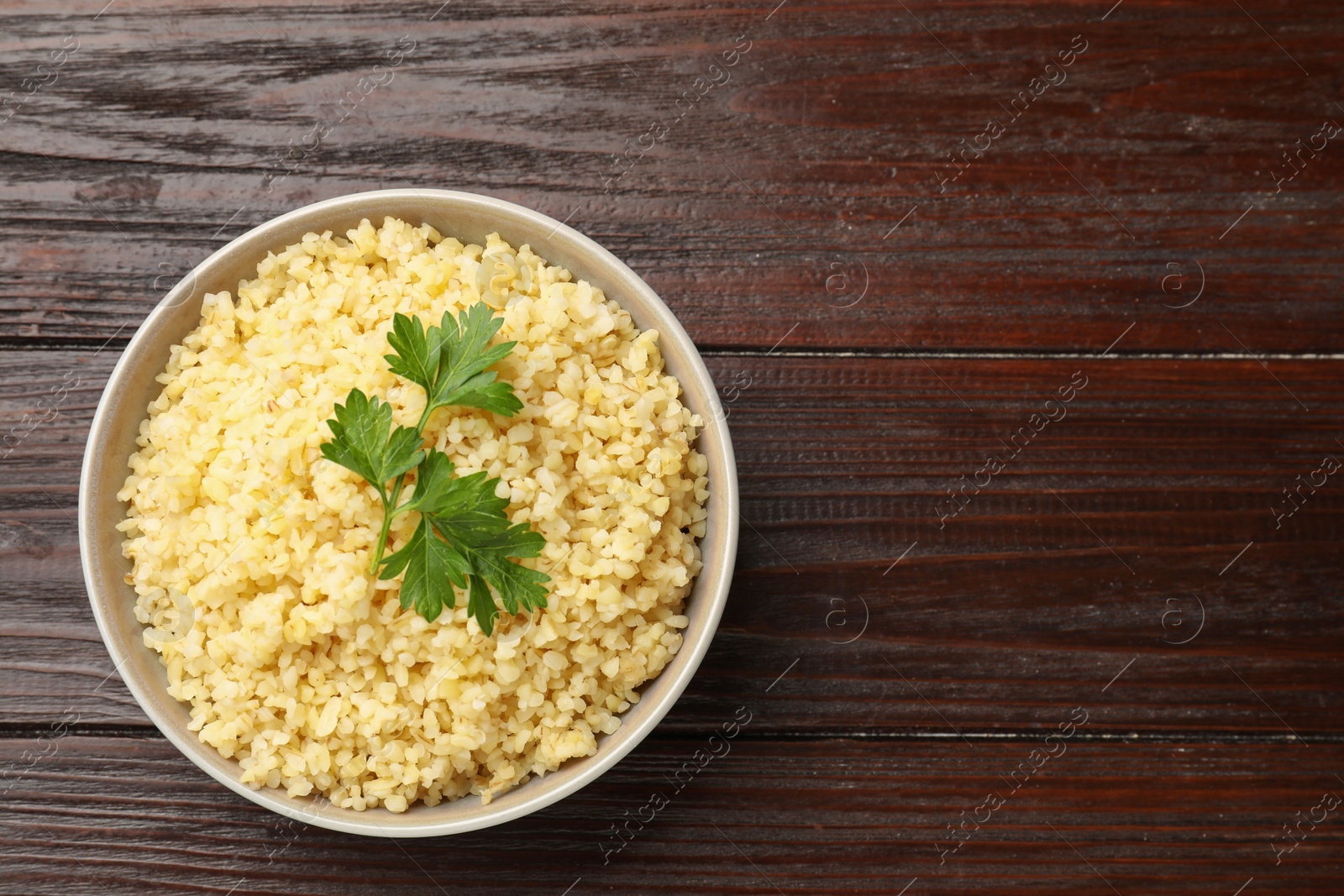 Photo of Delicious bulgur with parsley in bowl on wooden table, top view. Space for text