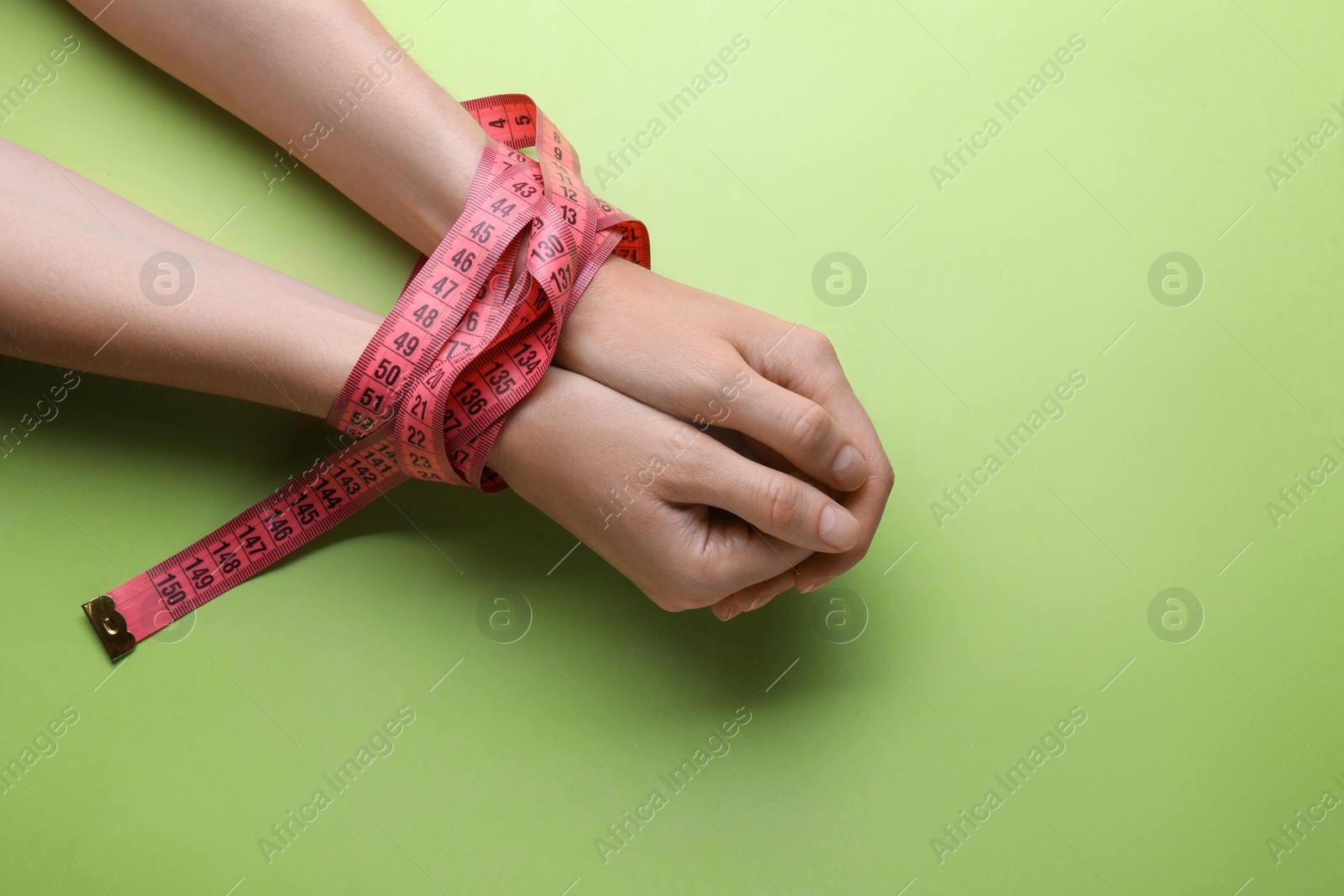 Photo of Woman tied with measuring tape on light green background, top view. Diet concept