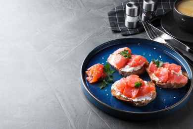 Photo of Tasty bruschettas with salmon, cream cheese and parsley on grey table, space for text