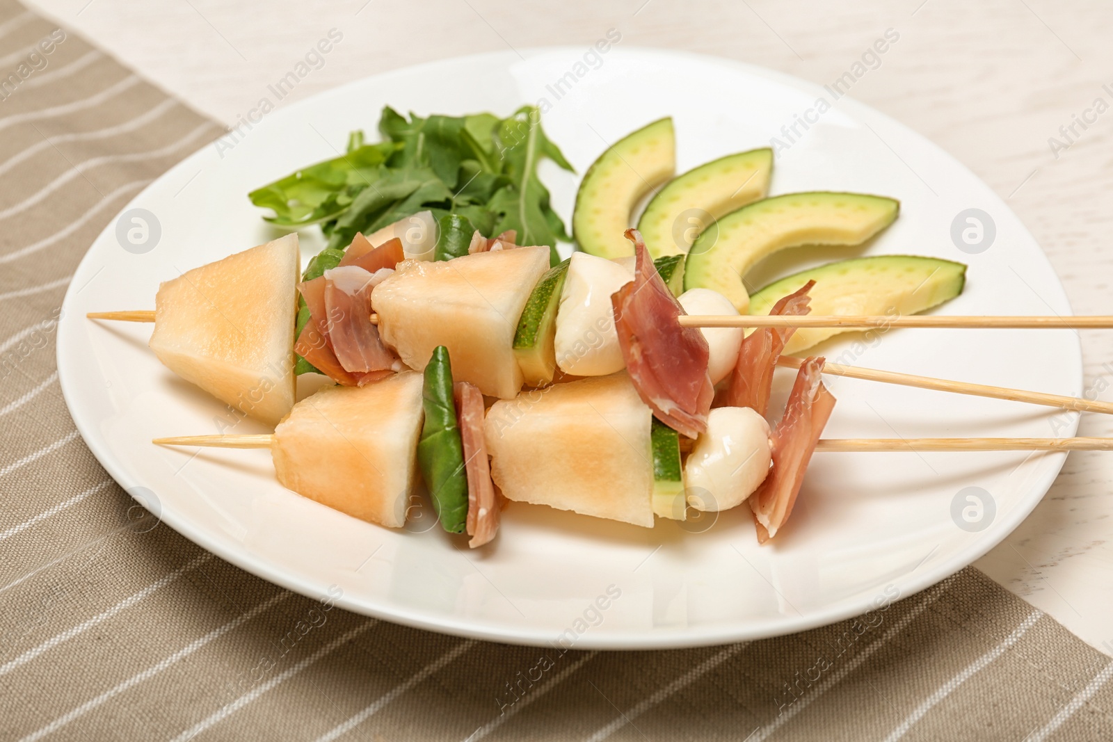 Photo of Plate with melon, mozzarella and prosciutto skewers on table