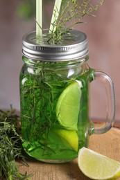 Mason jar of homemade refreshing tarragon drink with lemon slices and sprigs on wooden stump, closeup