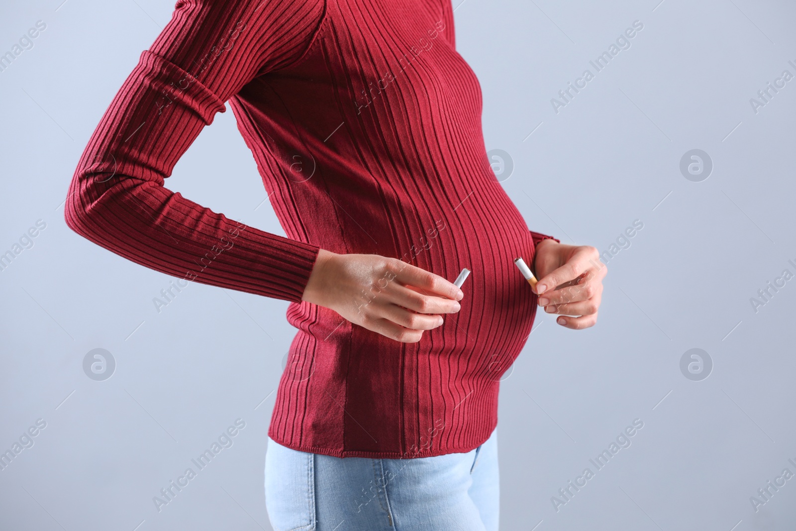 Photo of Young pregnant woman breaking cigarette on grey background, closeup. Harm to unborn baby