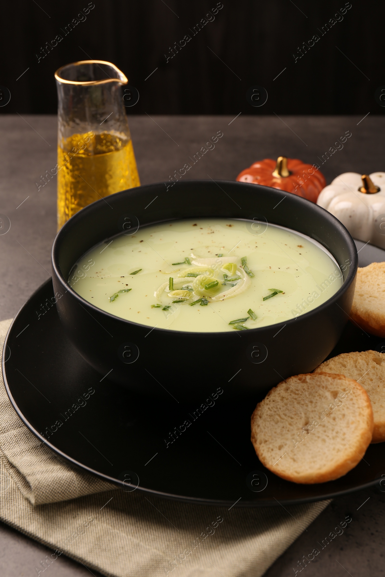 Photo of Bowl of tasty leek soup and bread on grey table, closeup