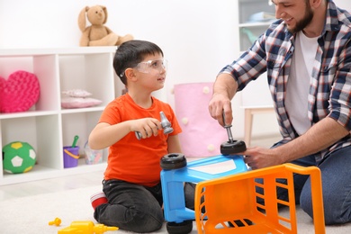 Photo of Man and his child as repairman playing with toy cart at home